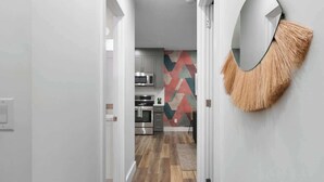 Ein Flur, der zu einer Küche mit modernen Geräten und einer Wand mit geometrischen Mustern führt.