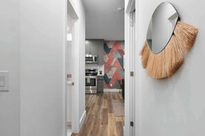 Ein Flur, der zu einer Küche mit modernen Geräten und einer Wand mit geometrischen Mustern führt.