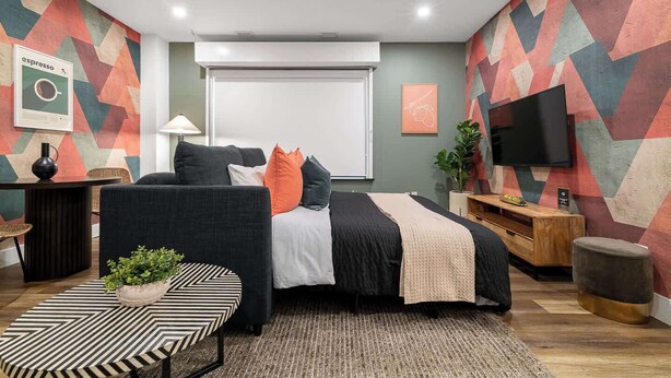 Ein modernes Schlafzimmer mit einem Bett, einem Schreibtisch, einem Fernseher und einem gemusterten Teppich.
