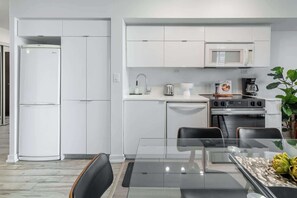 A compact kitchen with white cabinetry, a built-in microwave, a stove, and a sink. - Chic 2BR Downtown King Suite Parking Sleeps 6 (Toronto)