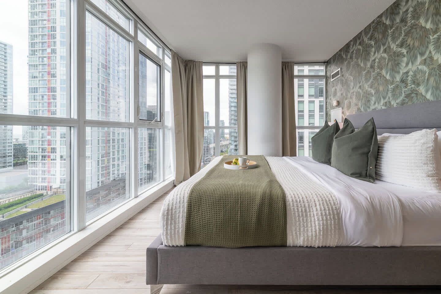 A modern hotel room with a large bed, a view of the cityscape, and a window with curtains.