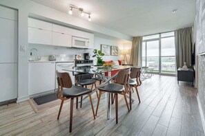 A modern kitchen with white cabinets, a glass dining table, and wooden chairs. - Chic 2BR Downtown King Suite Parking Sleeps 6 | Parking Available (Toronto)