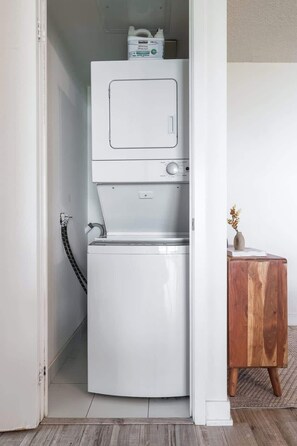 A compact, white laundry machine in a small room with a wooden side table and a vase. - Chic 2BR Downtown King Suite Parking Sleeps 6 (Toronto)