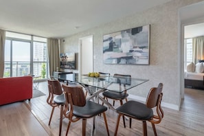 A modern living room with a glass dining table, wooden chairs, a red sofa, and a large abstract painting. - Chic 2BR Downtown King Suite Parking Sleeps 6 (Toronto)
