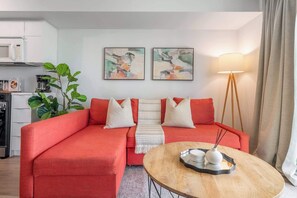 A living room with a red sofa, a round wooden coffee table, and two abstract paintings on the wall. - Chic 2BR Downtown King Suite Parking Sleeps 6 (Toronto)