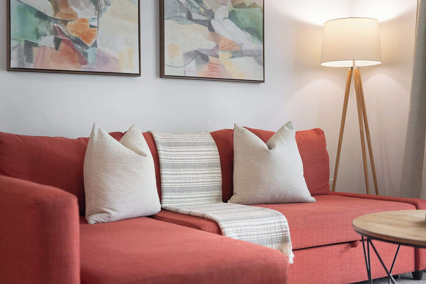 Un canapé rouge avec trois coussins, un plaid blanc et une lampe de sol avec un pied en bois.