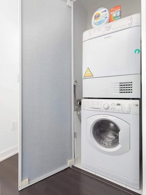 A front-loading washing machine with a control panel, a detergent bottle, and a box on top.