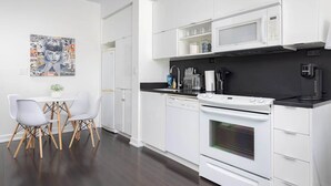 A modern kitchen with white cabinetry, a black countertop, a white stove, and a dining area with a white table and chairs.