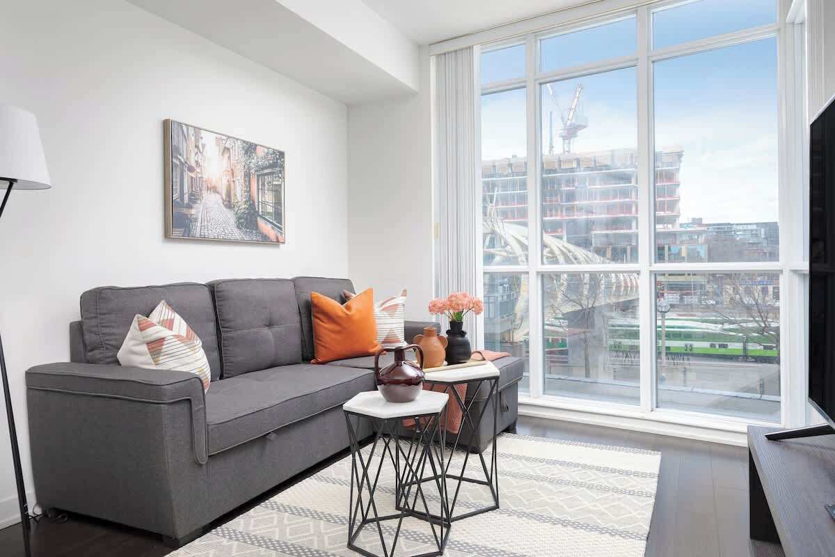 A modern living room with a grey sofa, a coffee table, and a large window offering a view of a cityscape.