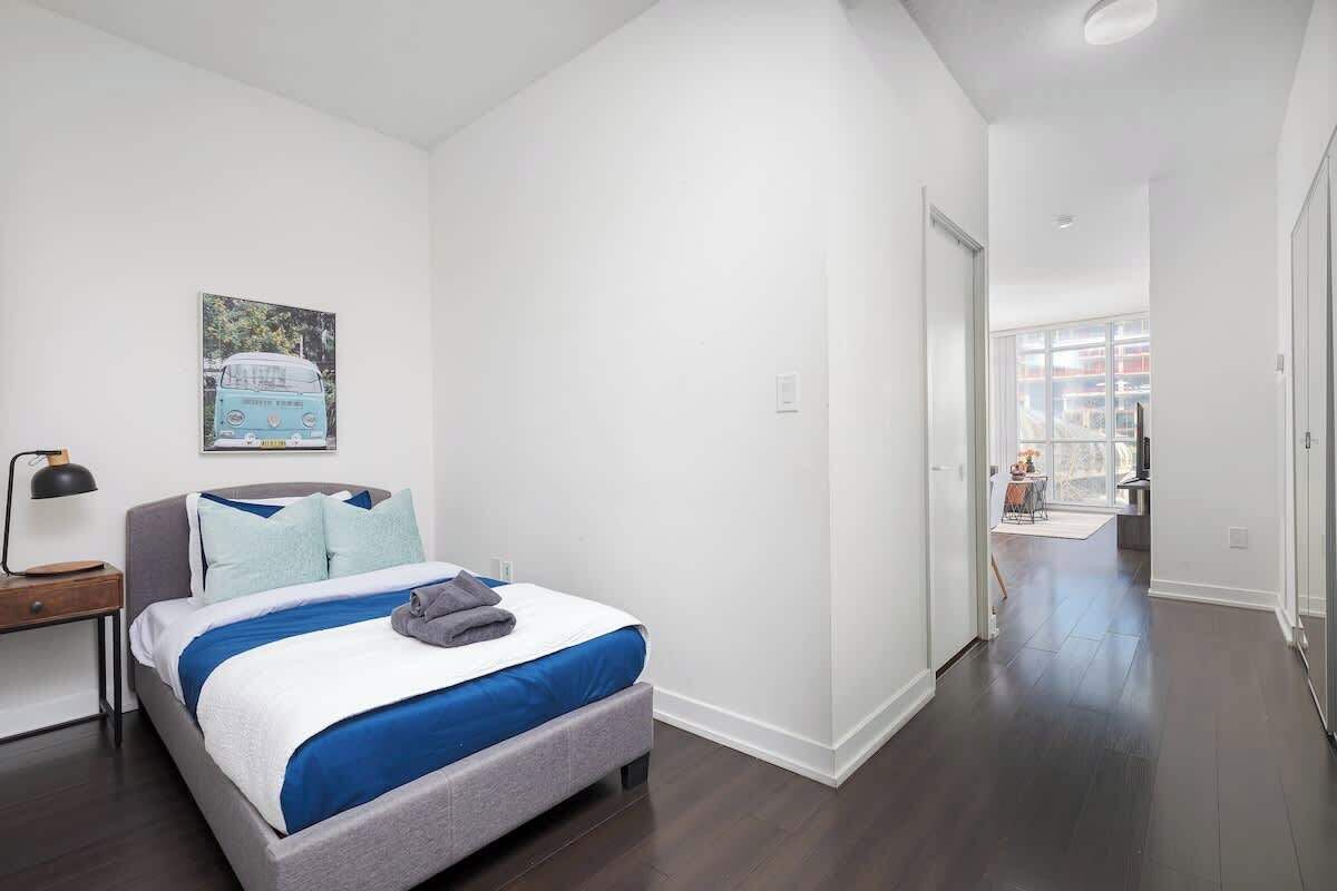 A modern hotel room with a large bed, a nightstand, a lamp, and a window with a view of the city.
