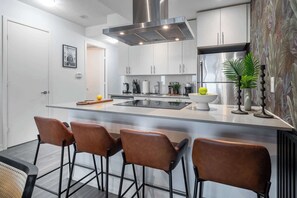 A modern kitchen with a central island, stainless steel appliances, and bar stools. - Waterfront Luxury  King Bed  Patio Games | Parking Available (Toronto)