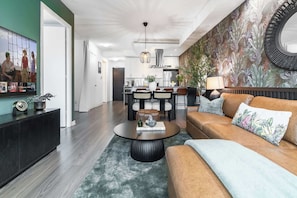 A modern living room with a brown leather sofa, a round coffee table, and a dining area with a chandelier. - Waterfront Luxury  King Bed  Patio Games | Parking Available (Toronto)