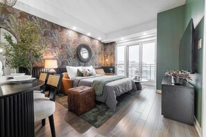 A modern hotel room with a large bed, a dining area, and a view of the city.