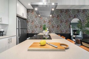 Een moderne keuken met een centraal eiland, roestvrijstalen apparatuur en een tropisch behangdesign.