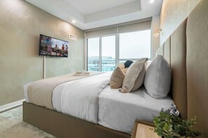 Ein modernes Schlafzimmer mit einem großen Bett, einem flachbildfernseher an der Wand und einem großen Fenster mit Blick auf die Stadt.