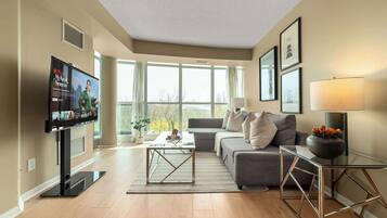 A modern living room with a flat-screen TV, a grey sofa, a glass coffee table, and a lamp.