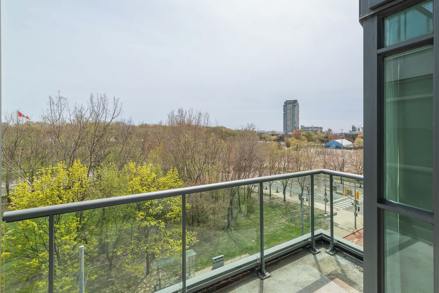 A balcony with a metal railing overlooking a park with trees and a distant building.