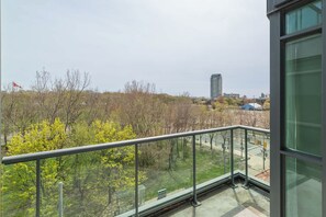 Un balcon doté d’une rambarde en métal, donnant sur un parc avec des arbres et un bâtiment situé au loin.