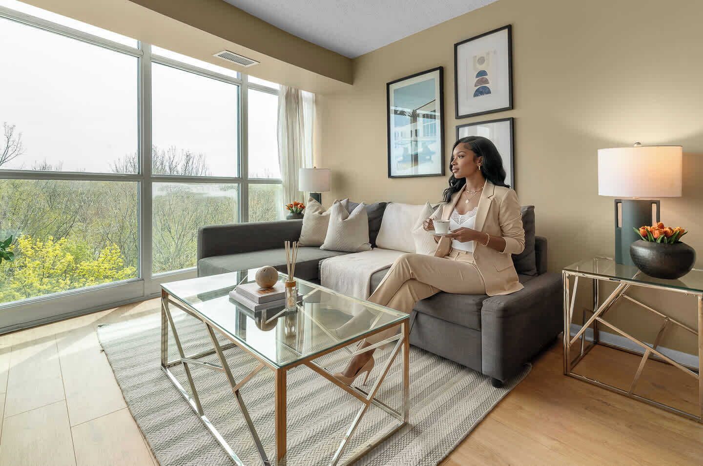 A modern living room with a sofa, a glass coffee table, and a view through large windows.