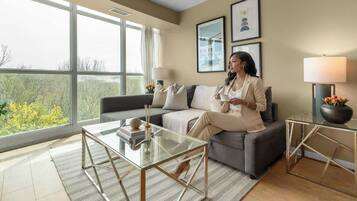 A modern living room with a sofa, a glass coffee table, and a view through large windows.