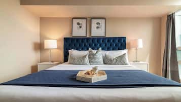 A hotel room with a large bed, two bedside tables with lamps, a headboard with a tufted design, and two framed pictures on the wall.
