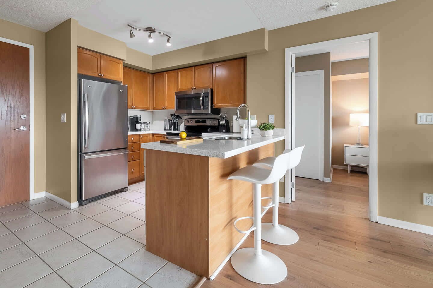 A modern kitchen with a central island, stainless steel appliances, wooden cabinets, and a bar stool.