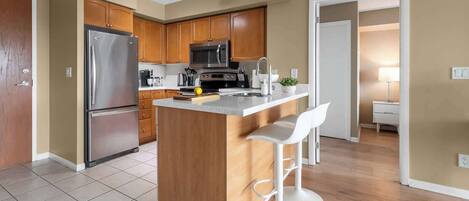 Una cocina moderna con una isla central, electrodomésticos de acero inoxidable, armarios de madera y un taburete de bar.