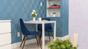 Un coin repas avec une table blanche et deux chaises bleues, un vase avec des fleurs et une étagère avec des livres et une plante.