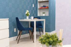 A dining area with a white table and two blue chairs, a vase with flowers, and a shelf with books and a plant. - Modern Basement Suite Heart of Ossington (Toronto)