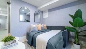 Une chambre à coucher moderne avec un lit, deux miroirs muraux, une plante en pot et une petite table sur laquelle se trouve un livre.