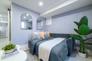 A modern bedroom with a bed, two wall mirrors, a potted plant, and a small table with a book. - Modern Basement Suite Heart of Ossington (Toronto)