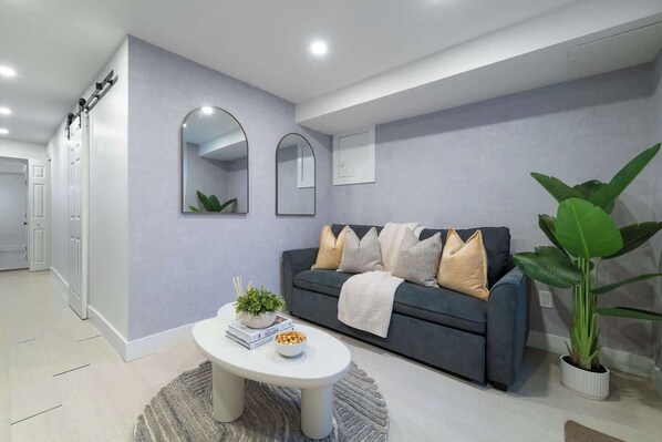 A modern living room with a grey sofa, a coffee table, and a large plant. - Modern Basement Suite Heart of Ossington (Toronto)