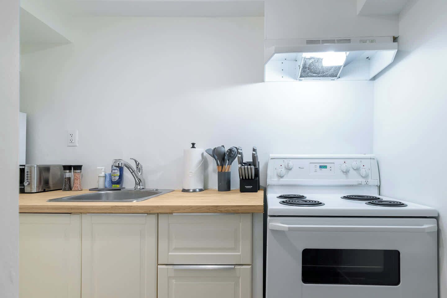 A kitchen with a white stove, a sink, and a countertop with various kitchen items.