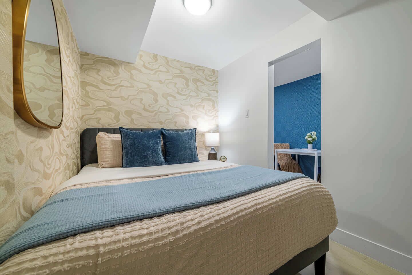 A bedroom with a bed, a bedside table, a lamp, and a mirror.