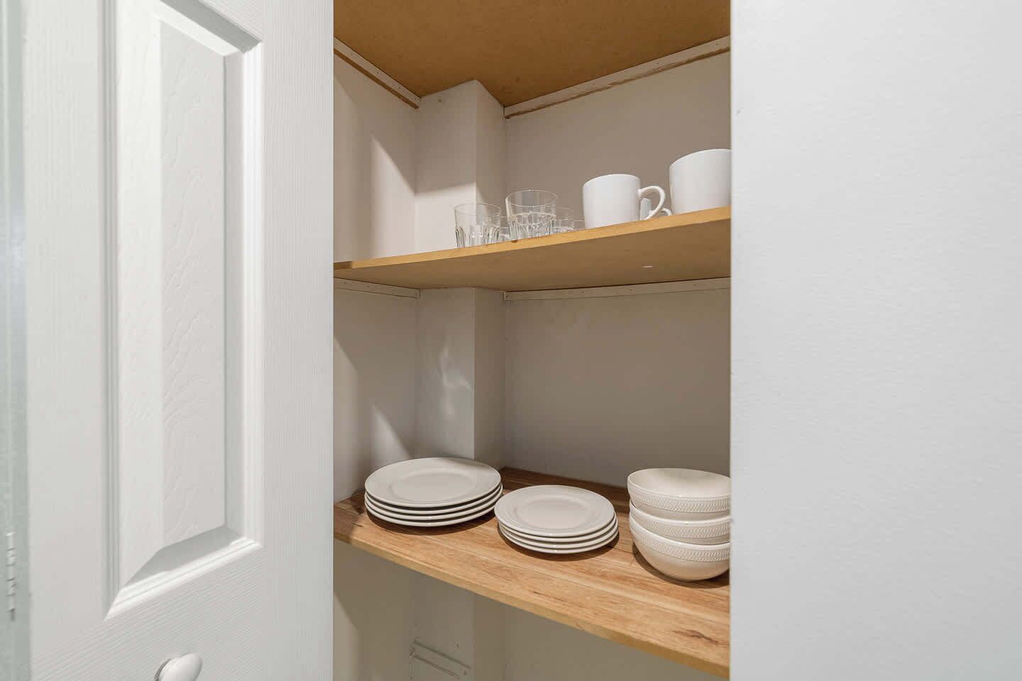 A white door with a wooden shelf above it containing plates and bowls.