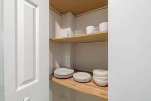 Une porte blanche surmontée d’une étagère en bois où sont rangées des assiettes et des bols.