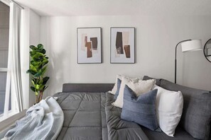 Una sala de estar moderna con un sofá gris, dos obras de arte abstracto en la pared, una lámpara de pie y una planta en maceta.