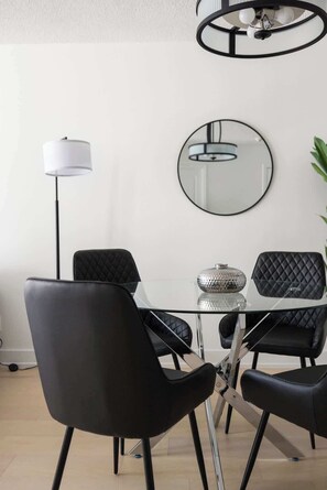 Un comedor moderno con una mesa de vidrio, sillas negras, una lámpara de pie y un espejo colgado en la pared.