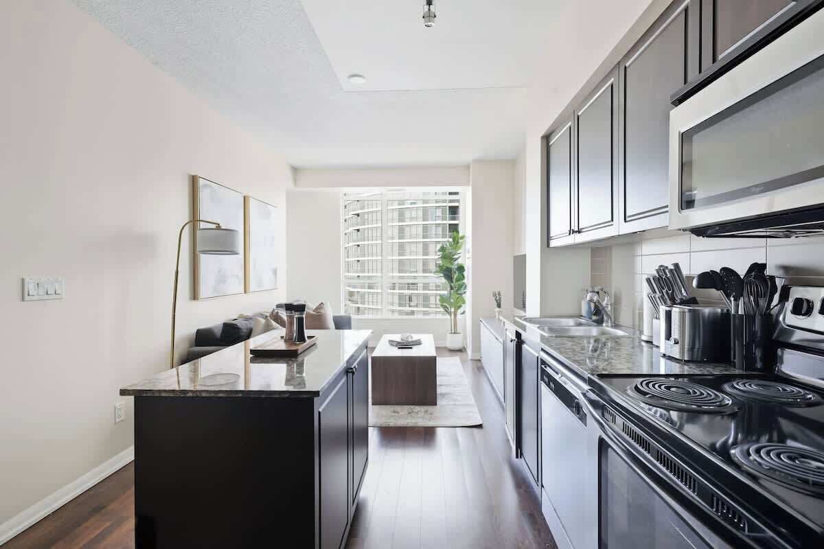 A modern kitchen with dark cabinetry, a black stove, and stainless steel appliances.