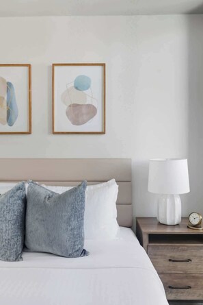 A neatly made bed with two pillows, a bedside table with a lamp, and two framed abstract paintings on the wall. - Urban Harbor Haven Modern 1BR Living Downtown | Parking Available (Toronto)
