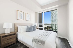 A bedroom with a bed, nightstands, a window with a city view, and framed artwork on the wall. - Urban Harbor Haven Modern 1BR Living Downtown | Parking Available (Toronto)