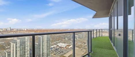 A balcony with a clear view of the cityscape, featuring high-rise buildings and a parking lot.