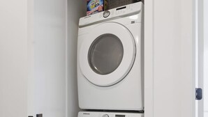A laundry room with two stacked washing machines and a shelf with laundry detergent.