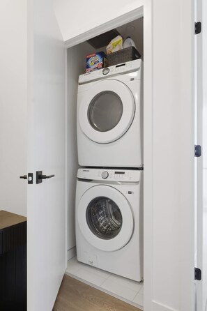 Une buanderie équipée de deux machines à laver superposées et d’une étagère où sont rangées les produits de lessive.
