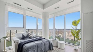 Un dormitorio moderno con una cama grande, varios ventanales y vista a la ciudad.