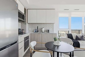 Une cuisine moderne dotée d’un four à micro-ondes encastré, un coin repas avec une table ronde et une vue sur l’extérieur grâce à de grandes fenêtres.