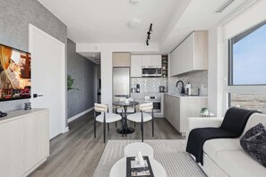 Eine moderne Küche mit weißen Schränken, eine Essecke mit rundem Tisch und Stühlen sowie ein Wohnbereich mit einer Couch und einem Couchtisch.