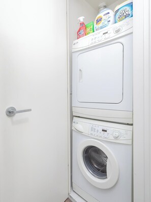 A laundry room with a washing machine and dryer, a door handle, and detergent bottles on top.