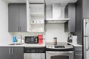 A modern kitchen with grey cabinets, a stainless steel refrigerator, a microwave, a coffee maker, and a dishwasher.