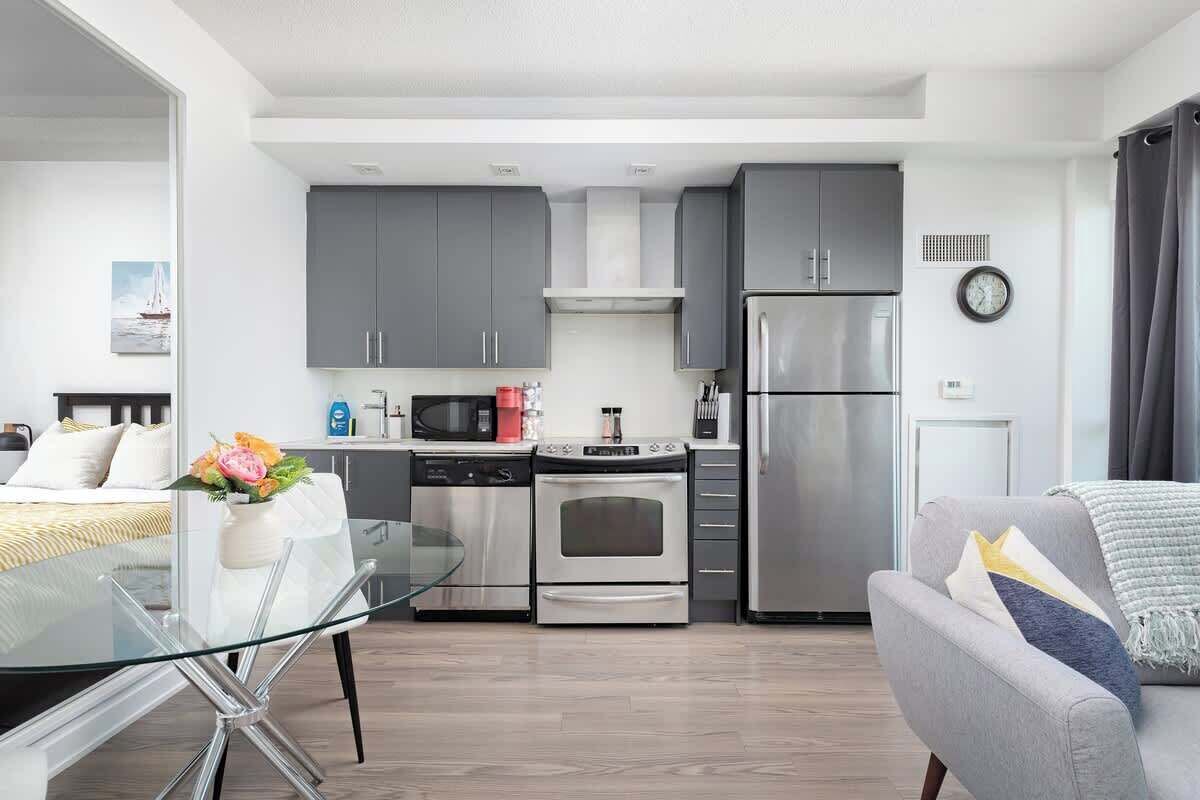 Una cocina moderna con armarios grises, un refrigerador de acero inoxidable y una mesa de comedor de vidrio.